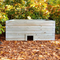 Wooden animal den and planter in a natural setting with trees and fallen leaves.