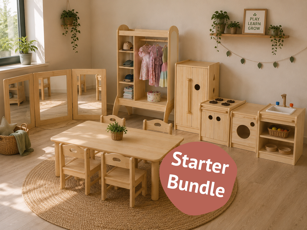 A children's wooden playroom starter bundle arranged in a bright room. The set includes a small wooden table and four matching chairs on a round woven rug, a wooden clothing rack with hanging garments, a wooden storage cabinet, a wooden play kitchen with a stove and sink, a wooden play dryer, and fold-out mirrors.